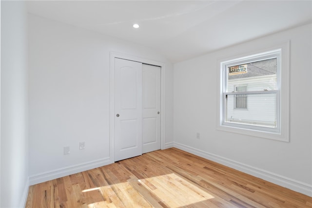unfurnished bedroom with a closet, baseboards, recessed lighting, lofted ceiling, and light wood-style floors