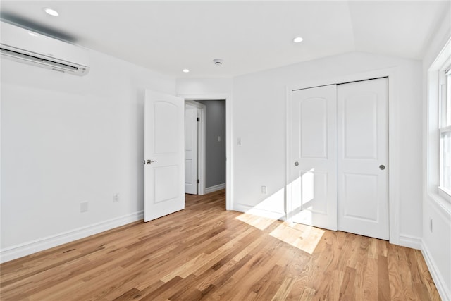 unfurnished bedroom with baseboards, light wood-type flooring, a closet, and an AC wall unit