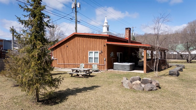 rear view of property featuring a chimney, central air condition unit, a hot tub, board and batten siding, and a lawn