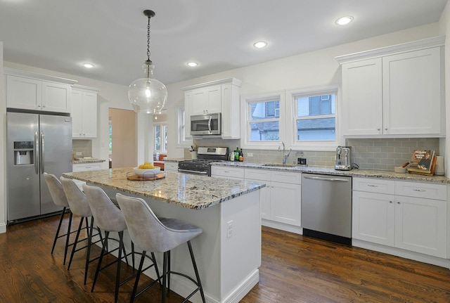 kitchen featuring appliances with stainless steel finishes, a sink, a center island, white cabinetry, and a breakfast bar