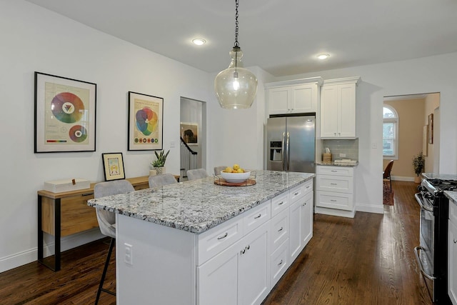 kitchen featuring stainless steel appliances, a breakfast bar area, dark wood-style floors, light stone counters, and white cabinetry