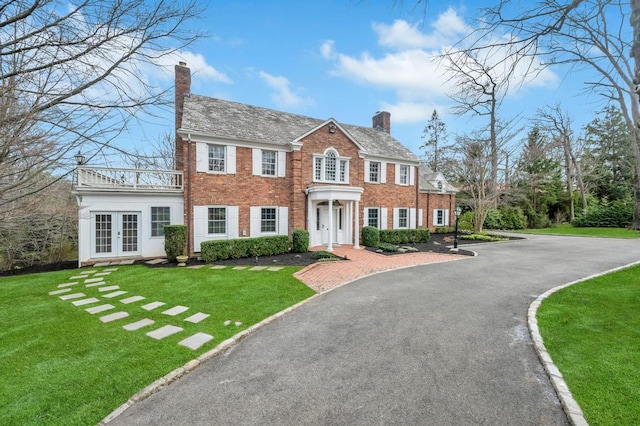 85 Station Rd, Great Neck, NY 11023 - view of front facade with driveway, a front yard, french doors, a chimney, and brick siding