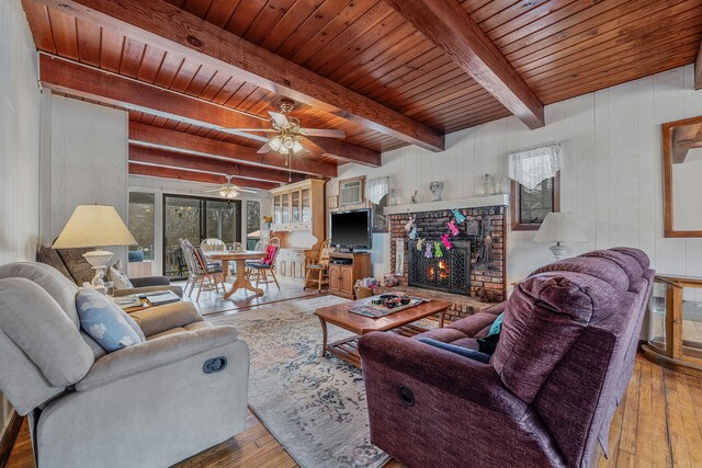 living room featuring wood ceiling, ceiling fan, a fireplace, wood-type flooring, and beamed ceiling
