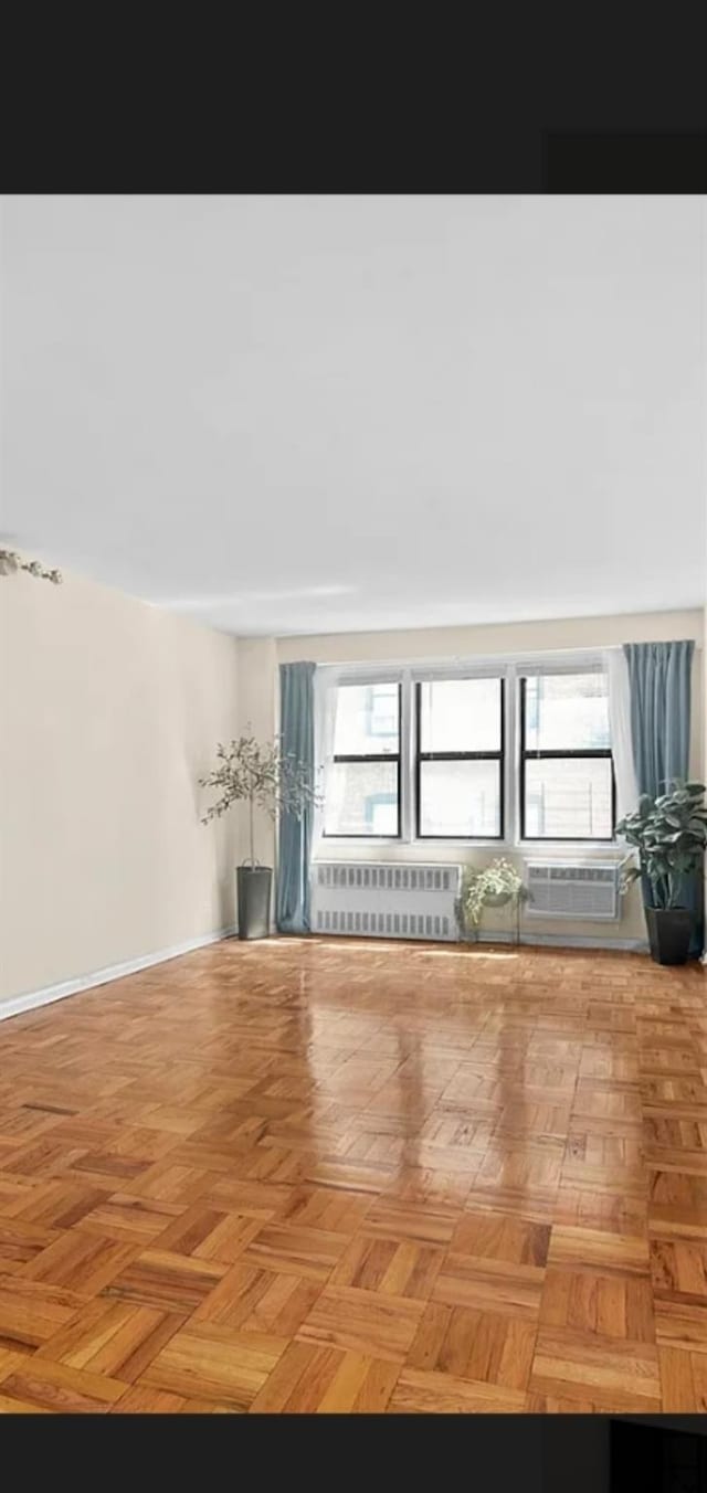 unfurnished living room featuring a wall mounted air conditioner, radiator heating unit, and a healthy amount of sunlight