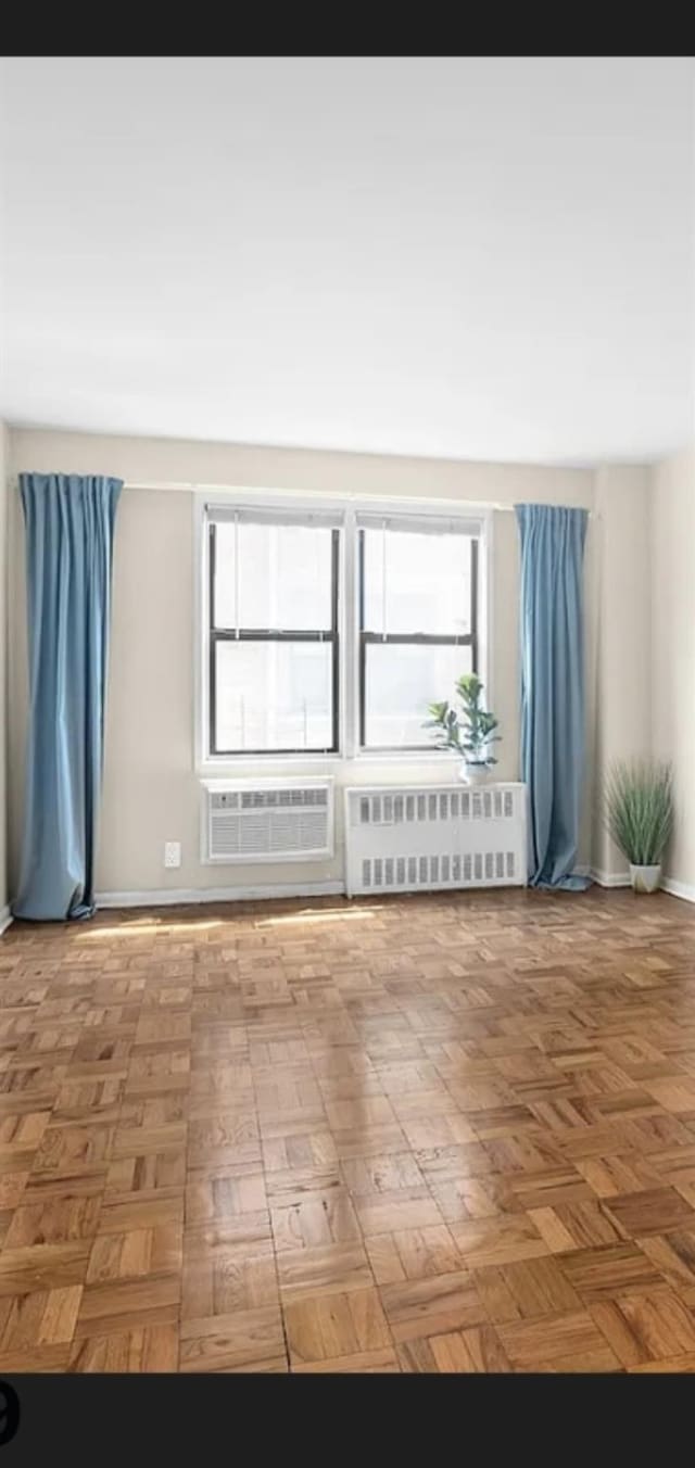 unfurnished room featuring baseboards, a wall mounted AC, and radiator heating unit