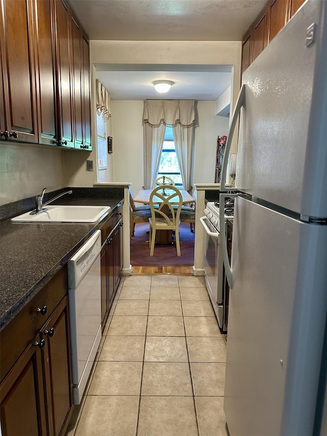 kitchen featuring a sink, dark countertops, light tile patterned floors, and white appliances