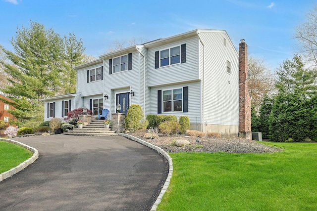 view of front facade with a chimney, cooling unit, aphalt driveway, and a front lawn