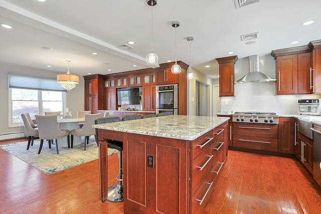 kitchen featuring wood finished floors, stainless steel appliances, wall chimney range hood, a center island, and visible vents