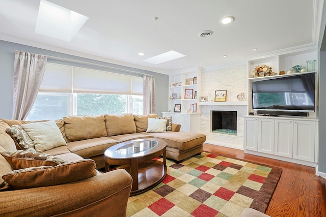 living area with light wood-style floors, built in features, crown molding, a stone fireplace, and a skylight