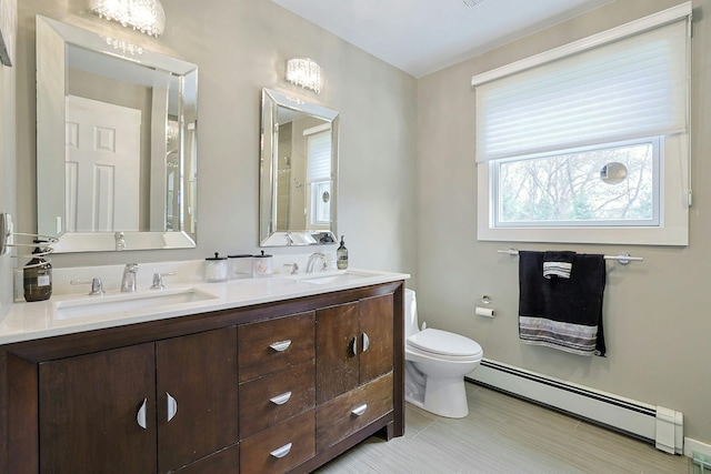 full bath featuring double vanity, toilet, baseboard heating, and a sink