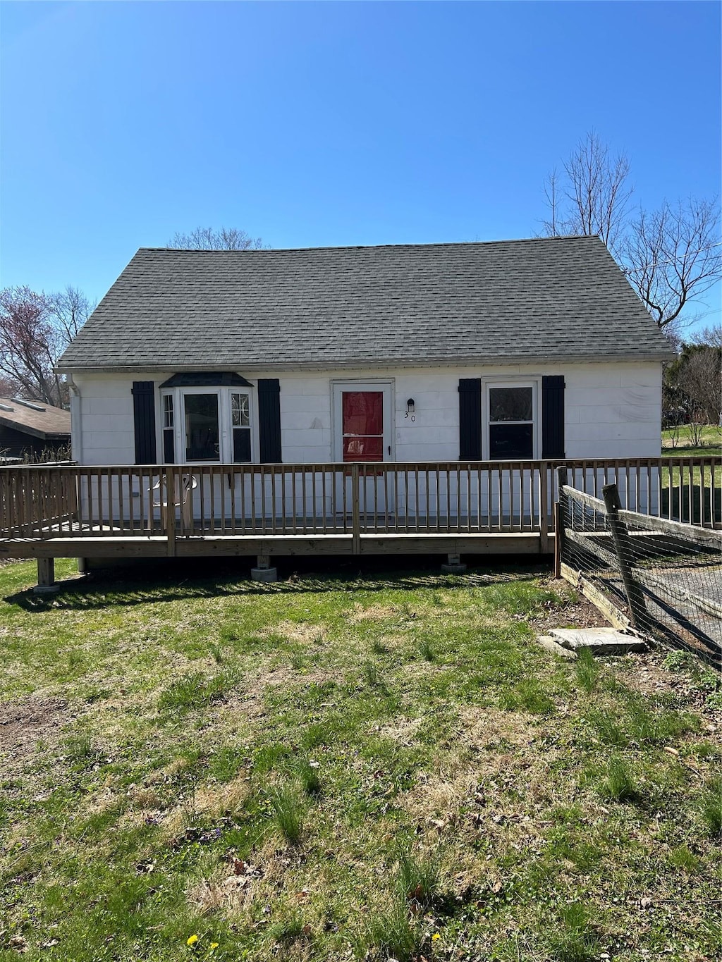 ranch-style house featuring a wooden deck, a shingled roof, and a front lawn