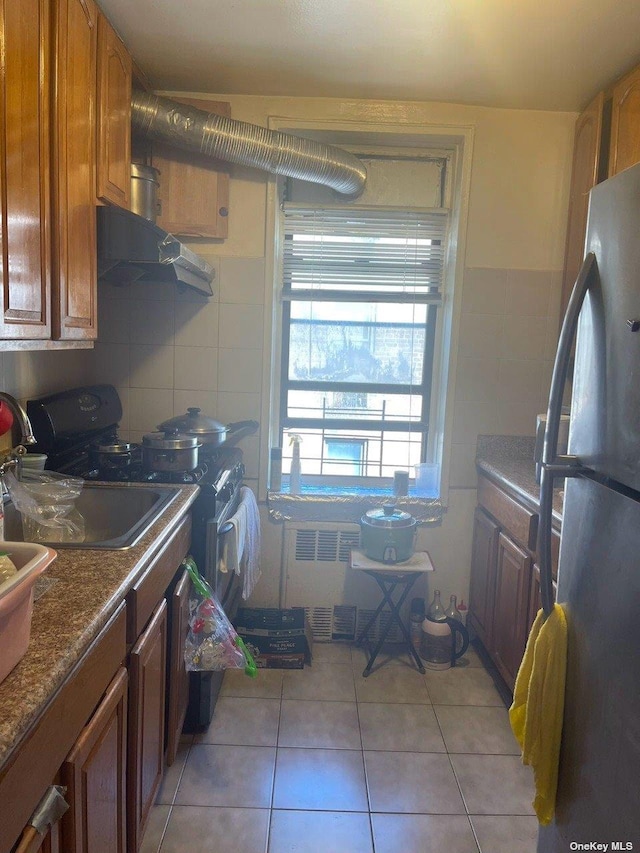141-05 Northern Blvd Unit 6K, Flushing, NY 11355 - kitchen with light tile patterned flooring, tile walls, radiator heating unit, under cabinet range hood, and freestanding refrigerator