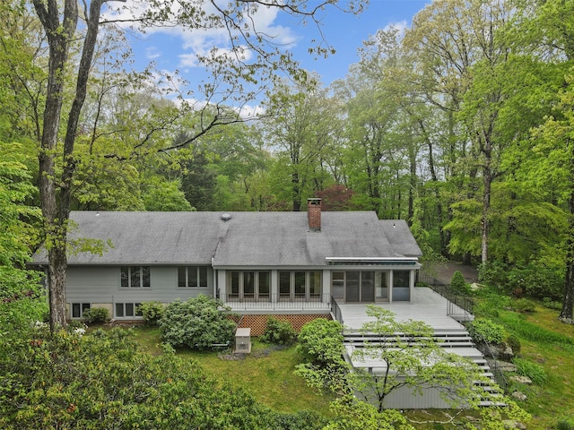 rear view of property featuring a sunroom, a chimney, and a wooden deck