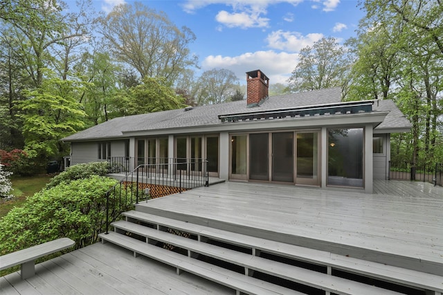 back of property with roof with shingles, a deck, a chimney, and a sunroom