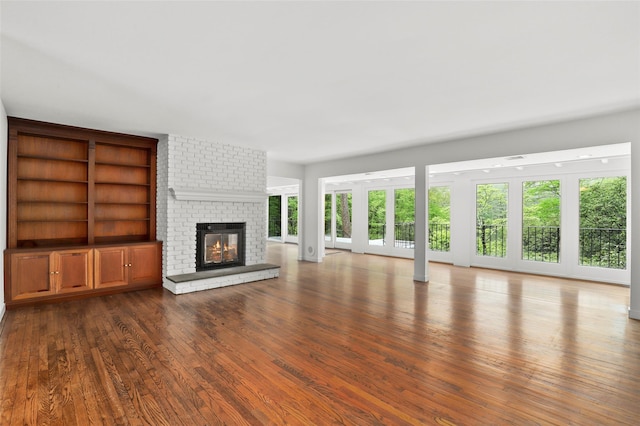 unfurnished living room with a fireplace, built in features, and wood finished floors