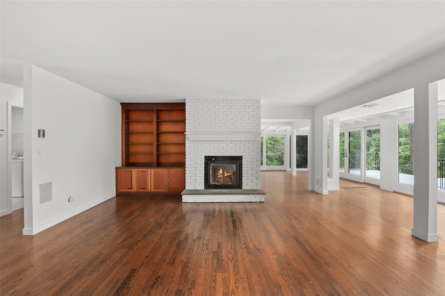 unfurnished living room with dark wood-style floors, a fireplace, baseboards, built in shelves, and washer / clothes dryer