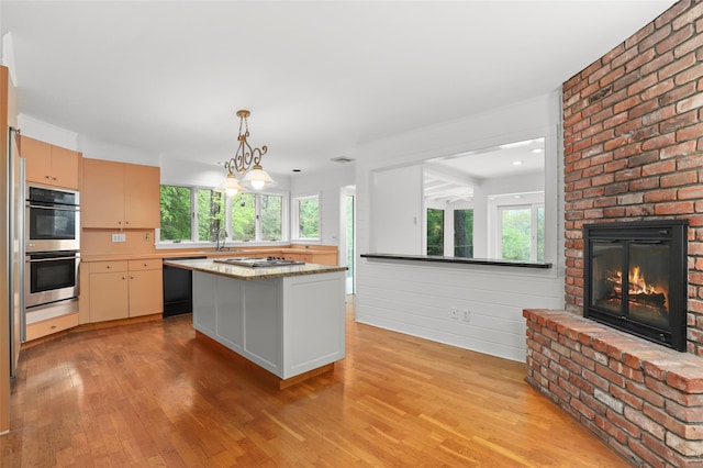kitchen with black dishwasher, stainless steel double oven, light wood finished floors, a brick fireplace, and healthy amount of natural light