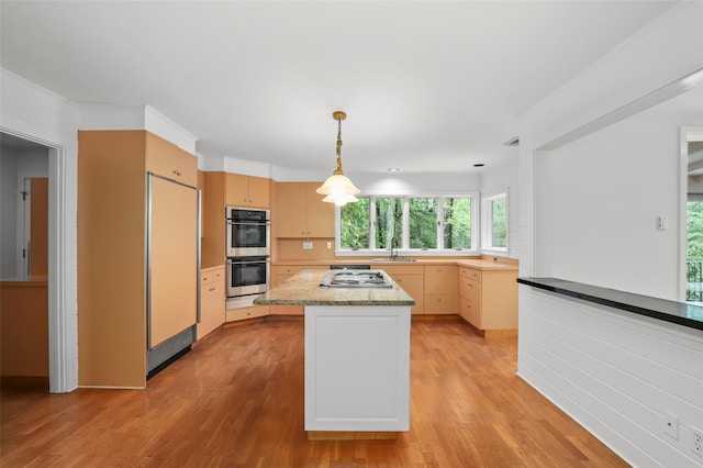 kitchen featuring stainless steel appliances, a sink, light wood-style floors, light brown cabinetry, and decorative light fixtures