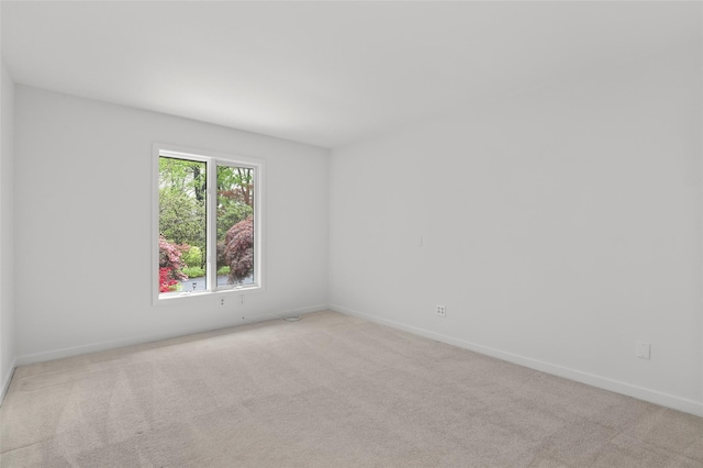 spare room featuring light colored carpet and baseboards