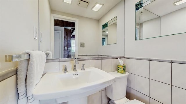 half bath featuring a sink, toilet, tile walls, wainscoting, and visible vents