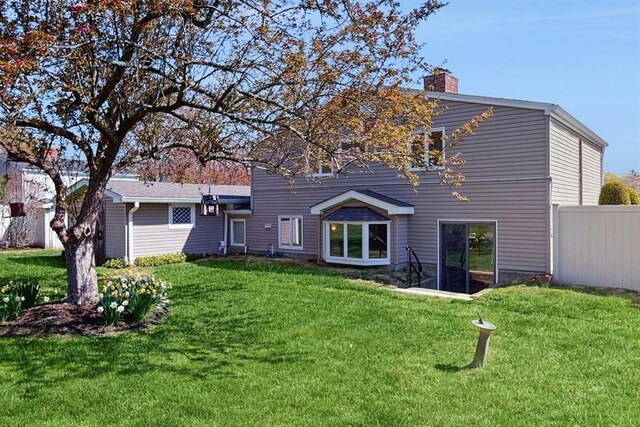 back of house featuring a lawn, fence, and a chimney