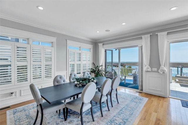 dining room featuring a decorative wall, plenty of natural light, ornamental molding, and light wood finished floors