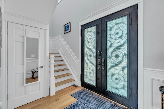 entryway with stairway, a decorative wall, french doors, and light wood-style floors