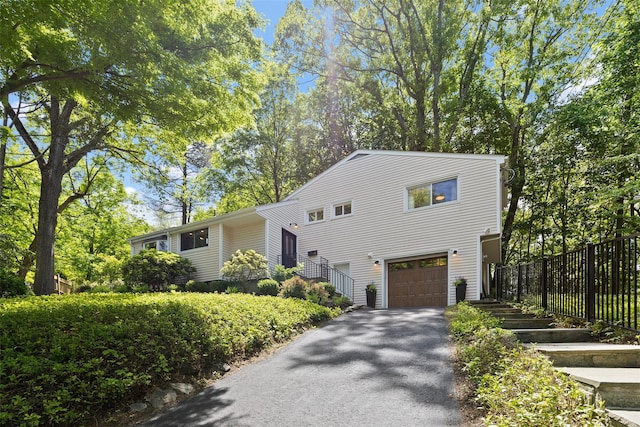 view of front of home with a garage, asphalt driveway, and fence