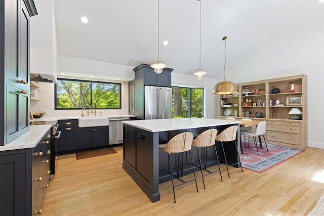 kitchen with appliances with stainless steel finishes, a kitchen bar, light countertops, light wood-style floors, and a sink