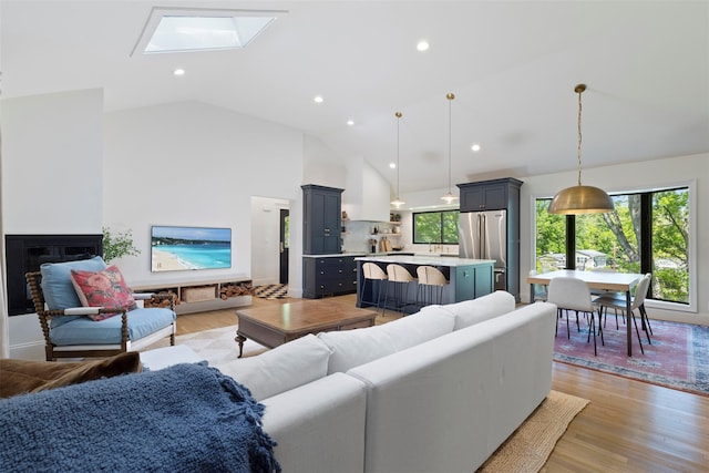 living area featuring a skylight, light wood-type flooring, recessed lighting, and high vaulted ceiling