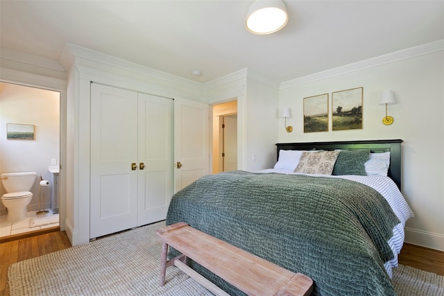 bedroom with wood finished floors, ornamental molding, a closet, baseboards, and connected bathroom