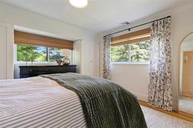 bedroom with wood finished floors, multiple windows, and ornamental molding