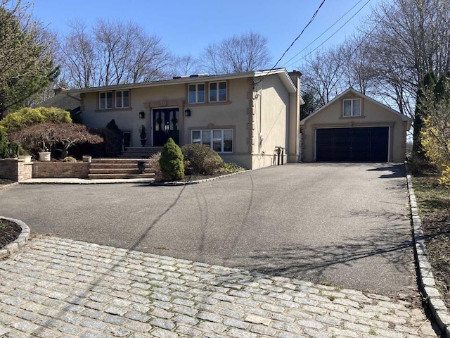 bi-level home featuring stucco siding, an outdoor structure, and aphalt driveway