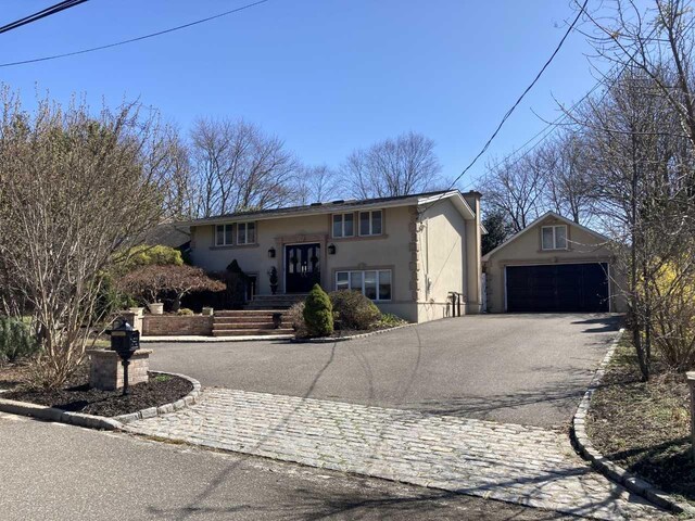 split foyer home featuring stucco siding, a garage, driveway, and an outbuilding