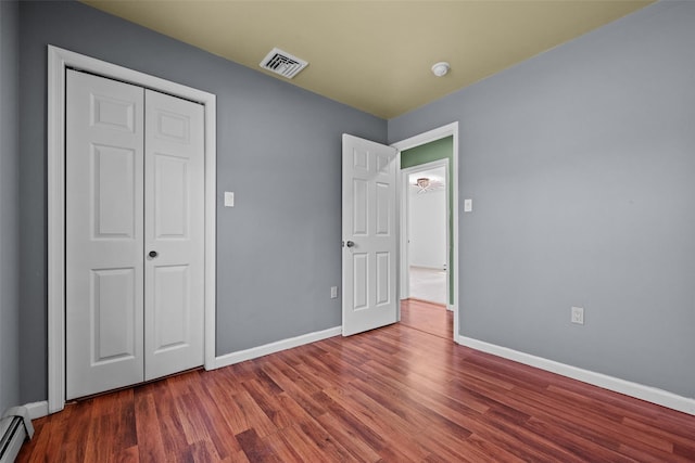 unfurnished bedroom with baseboards, visible vents, a baseboard radiator, a closet, and wood finished floors