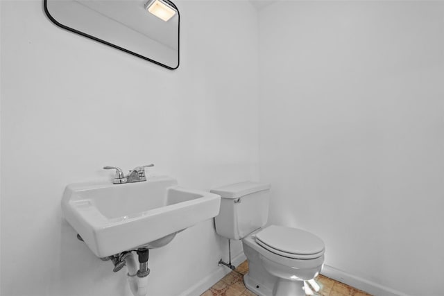 bathroom featuring baseboards, toilet, and a sink