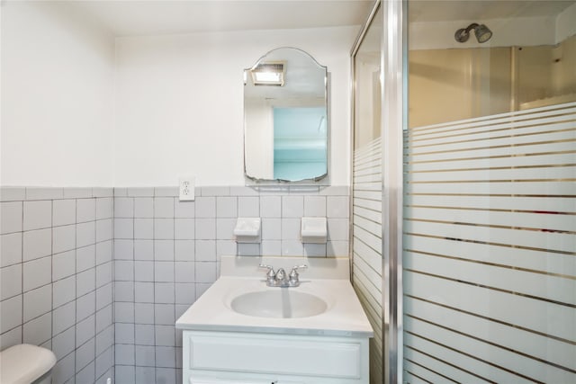 full bathroom featuring tile walls, toilet, a shower stall, vanity, and wainscoting