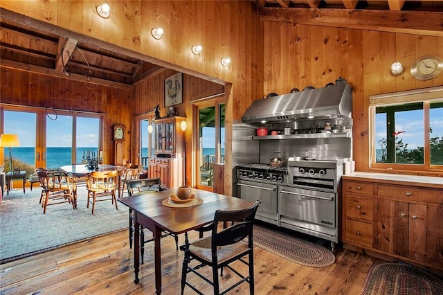 1635 Isabella Beach Rd, Fishers Island, NY 06390 - kitchen with extractor fan, wood walls, double oven range, hardwood / wood-style floors, and brown cabinetry