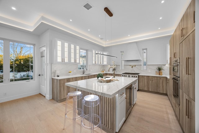 kitchen with premium range hood, backsplash, a raised ceiling, a sink, and visible vents