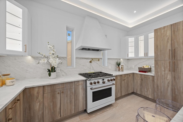 kitchen featuring light wood finished floors, white cabinetry, tasteful backsplash, custom range hood, and white range with gas stovetop