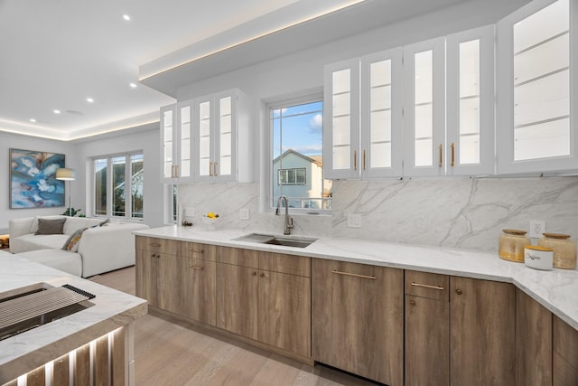 kitchen with open floor plan, light wood-type flooring, a sink, light stone countertops, and glass insert cabinets