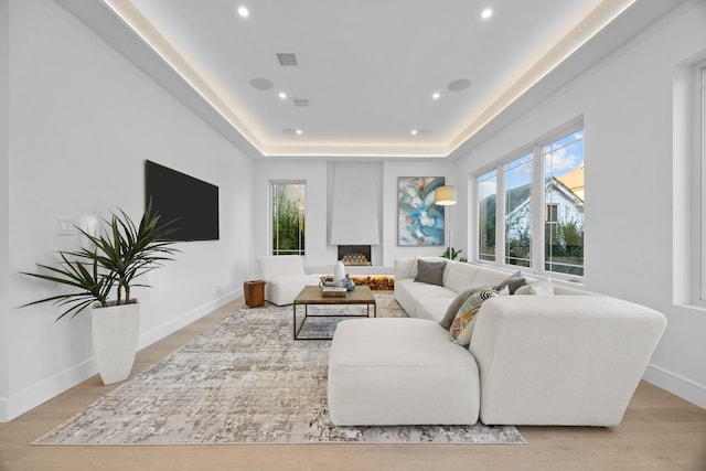 living room featuring a raised ceiling, light wood-type flooring, baseboards, visible vents, and recessed lighting