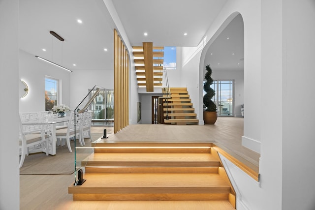 staircase with wood finished floors, arched walkways, and recessed lighting