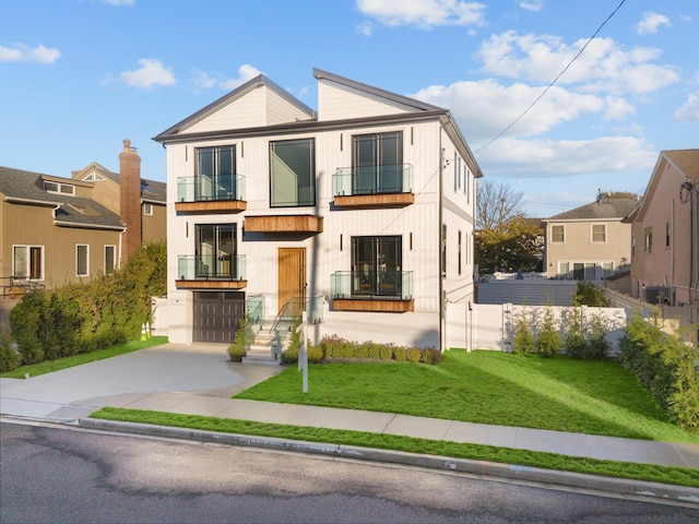 view of front of property featuring a balcony, fence, an attached garage, a front yard, and driveway