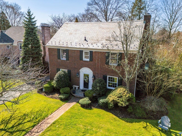 view of front of home featuring a front lawn, a chimney, and a high end roof
