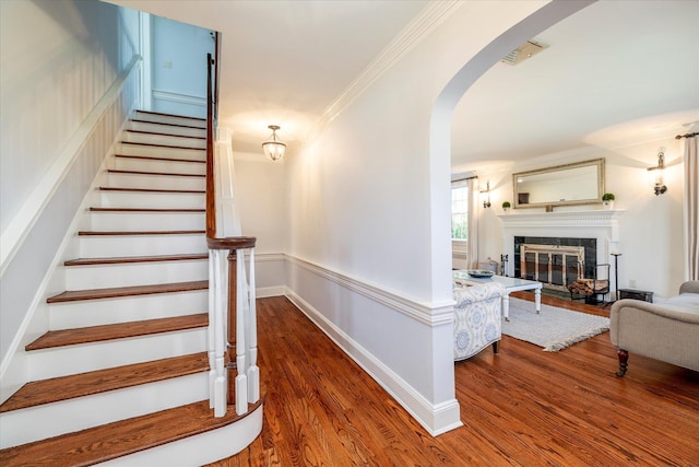 staircase featuring arched walkways, a glass covered fireplace, visible vents, wood finished floors, and crown molding