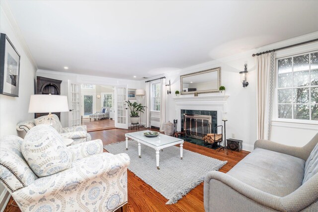 living room featuring wood finished floors, a fireplace, baseboards, ornamental molding, and recessed lighting
