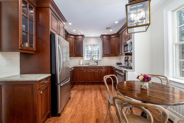 kitchen with stainless steel appliances, light wood-style flooring, visible vents, decorative backsplash, and glass insert cabinets