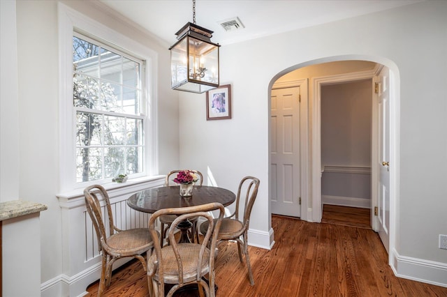 dining space with a wealth of natural light, wood finished floors, visible vents, and arched walkways