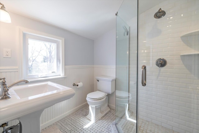 bathroom with a stall shower, a wainscoted wall, a sink, and toilet